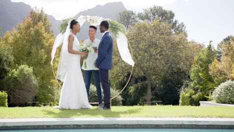 Biracial-man-officiating-wedding-of-african-american-couple-in-sunny-garden,-copy-space,-slow-motion
