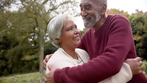 Happy-senior-biracial-couple-embracing-and-smiling-in-garden,-unaltered,-in-slow-motion