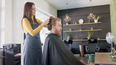 Caucasian-female-hairdresser-untying-long-hair-of-male-client-at-hair-salon,-in-slow-motion