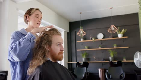 Happy-caucasian-female-hairdresser-advising-male-client-with-long-hair-at-salon,-in-slow-motion