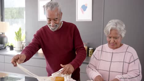 Älteres-Gemischtrassiges-Paar-Packt-Lebensmittel-In-Der-Küche-Aus,-Unverändert,-In-Zeitlupe