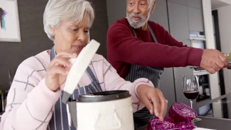 Senior-biracial-couple-cooking-dinner-and-cleaning-waste-in-kitchen,-unaltered,-in-slow-motion