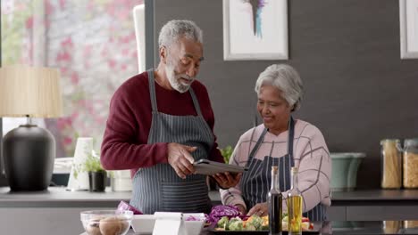 Älteres-Gemischtrassiges-Paar-Kocht-Abendessen-Und-Benutzt-Tablet-In-Der-Küche,-Unverändert,-In-Zeitlupe