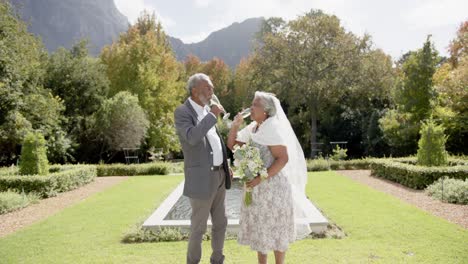 Happy-senior-biracial-couple-drinking-champagne-at-wedding-in-garden,-slow-motion