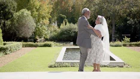 Happy-senior-biracial-couple-dancing-at-wedding-in-garden,-copy-space,-slow-motion