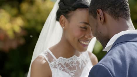 Afroamerikanisches-Paar-Lächelt-Und-Berührt-Köpfe-Bei-Ihrer-Hochzeit-Im-Sonnigen-Garten,-Zeitlupe