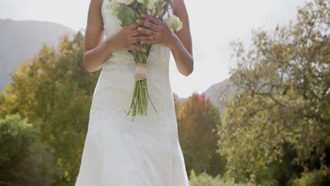 Glückliche-Afroamerikanische-Braut,-Die-Bei-Ihrer-Hochzeit-Im-Sonnigen-Garten-Einen-Blumenstrauß-Hält,-Zeitlupe