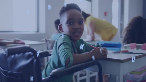 Animation-of-numbers-over-happy-african-american-schoolboy-in-wheelchair-at-desk-in-class