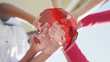 Animation-of-globe-over-diverse-schoolchildren-stacking-hands-outdoors