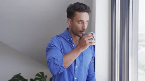 Portrait-of-biracial-man-drinking-coffee,-looking-out-of-window-and-smiling-to-camera,-slow-motion