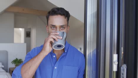 Portrait-of-happy-biracial-man-drinking-coffee-and-smiling-by-window,-slow-motion