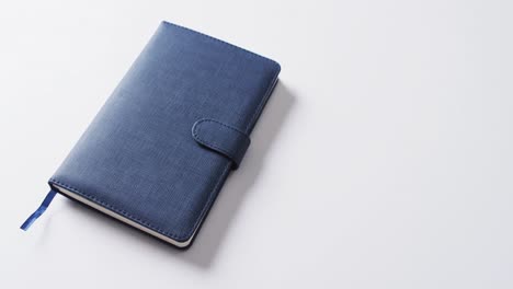 Close-up-of-closed-blue-notebook-with-copy-space-on-white-background-in-slow-motion
