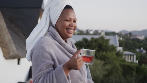 Happy-african-american-plus-size-woman-drinking-tea-on-balcony,-unaltered,-slow-motion
