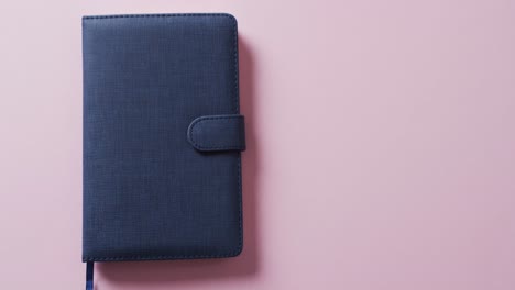 Nahaufnahme-Eines-Geschlossenen-Blauen-Notizbuchs-Mit-Kopierraum-Auf-Rosa-Hintergrund-In-Zeitlupe
