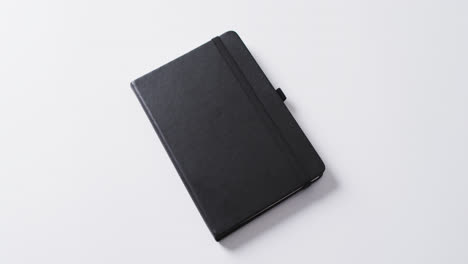 Nahaufnahme-Eines-Geschlossenen-Schwarzen-Notizbuchs-Mit-Kopierraum-Auf-Weißem-Hintergrund-In-Zeitlupe