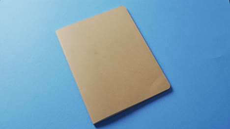 Nahaufnahme-Eines-Geschlossenen-Braunen-Buches-Mit-Kopierraum-Auf-Blauem-Hintergrund-In-Zeitlupe