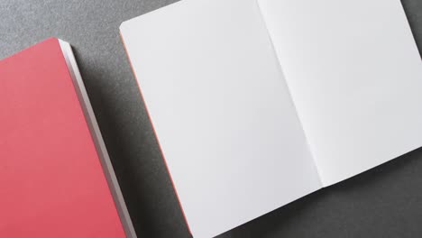 Close-up-of-open-blank-book-and-pink-book-with-copy-space-on-gray-background-in-slow-motion