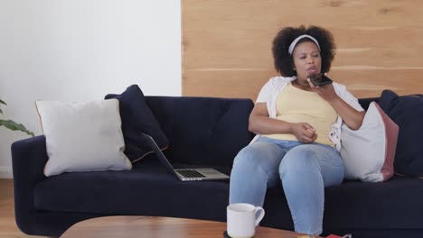 African-american-plus-size-woman-sitting-on-sofa-and-talking-on-smartphone,-unaltered,-slow-motion