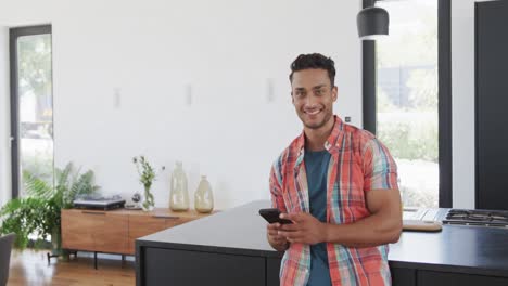 Portrait-of-happy-biracial-man-holding-smartphone-in-sunny-modern-apartment,-slow-motion