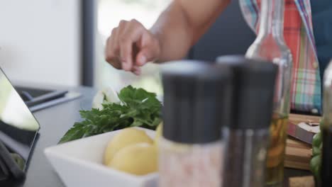 Midsection-of-biracial-man-using-tablet-and-chopping-vegetables-in-kitchen,-slow-motion