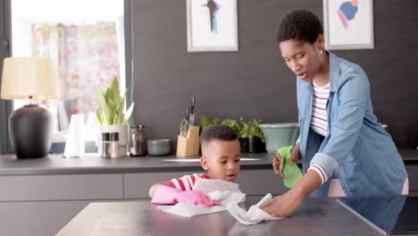 African-american-mother-and-son-cleaning-countertop-in-kitchen,-slow-motion