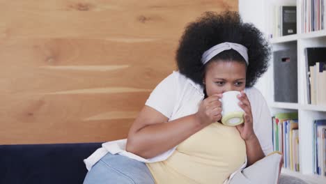 Thoughtful-african-american-plus-size-woman-holding-mug-and-drinking,-unaltered,-slow-motion