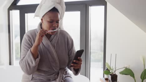 African-american-plus-size-woman-brushing-teeth-and-using-smartphone,-unaltered,-slow-motion