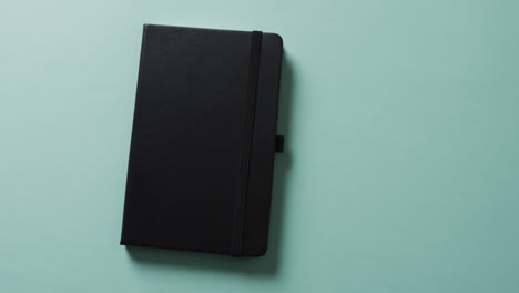 Close-up-of-closed-black-notebook-with-copy-space-on-green-background-in-slow-motion