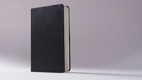 Close-up-of-open-black-book-standing-vertical-with-copy-space-on-white-background-in-slow-motion