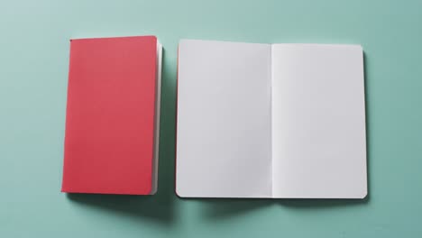 Close-up-of-open-blank-book-and-closed-red-book-with-copy-space-on-green-background-in-slow-motion