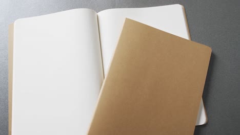Close-up-of-open-blank-book-and-brown-notebook-with-copy-space-on-gray-background-in-slow-motion