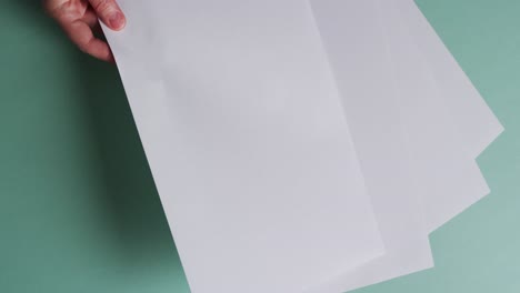 Hand-holding-piece-of-paper-over-pieces-of-paper-with-copy-space-on-green-background-in-slow-motion