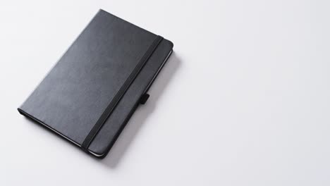 Close-up-of-closed-black-notebook-with-copy-space-on-white-background-in-slow-motion