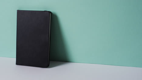 Close-up-of-closed-black-book-leaning-on-wall-with-copy-space-on-green-background-in-slow-motion