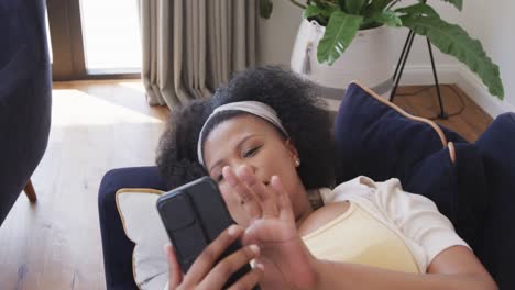 African-american-plus-size-woman-lying-on-sofa-and-using-smartphone,-unaltered,-in-slow-motion