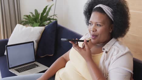 African-american-plus-size-woman-sitting-on-sofa-and-talking-on-smartphone,-unaltered,-slow-motion