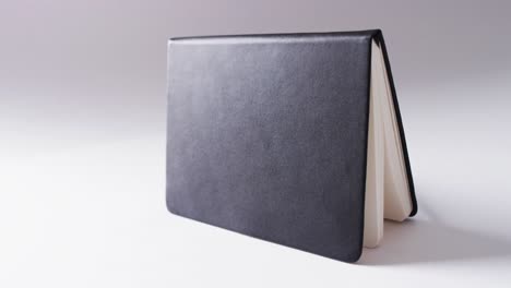 Close-up-of-open-black-book-standing-horizontal-with-copy-space-on-white-background-in-slow-motion