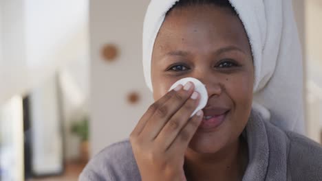 Happy-african-american-plus-size-woman-using-cotton-pad-for-cleansing-face,-unaltered,-slow-motion