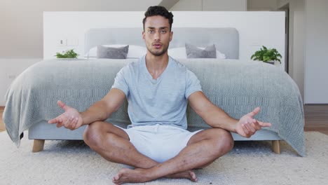 Relaxed-biracial-man-sitting-on-floor-in-bedroom-practicing-yoga-meditation,-slow-motion