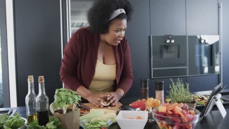 African-american-plus-size-woman-cooking-in-kitchen-and-using-tablet,-unaltered,-slow-motion