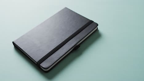 Close-up-of-closed-black-notebook-with-copy-space-on-green-background-in-slow-motion