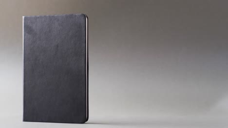 Close-up-of-closed-black-book-standing-vertical-with-copy-space-on-gray-background-in-slow-motion