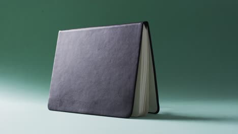 Close-up-of-open-black-book-standing-horizontal-with-copy-space-on-green-background-in-slow-motion