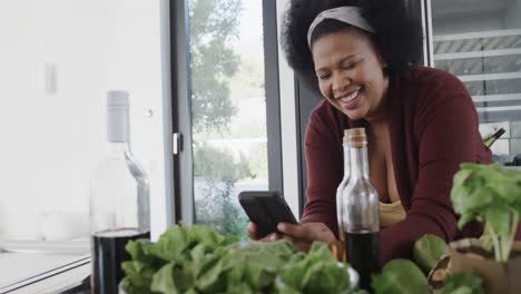 Happy-african-american-plus-size-woman-using-smartphone-in-kitchen,-unaltered,-slow-motion