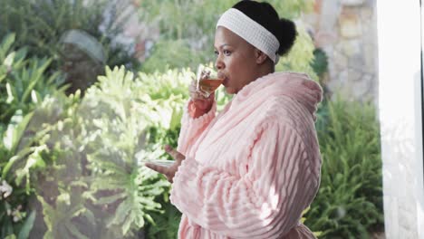 African-american-plus-size-woman-wearing-bathrobe-and-drinking-tea-at-spa,-unaltered,-slow-motion