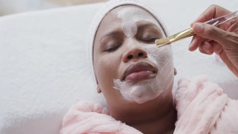 Kosmetikerin-Trägt-Schönheitsmaske-Auf-Das-Gesicht-Einer-Afroamerikanischen-Frau-In-Übergröße-Auf,-Unverändert,-Zeitlupe