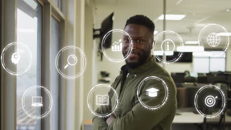 Animation-of-multiple-digital-icons-against-african-american-man-with-arms-crossed-smiling-at-office