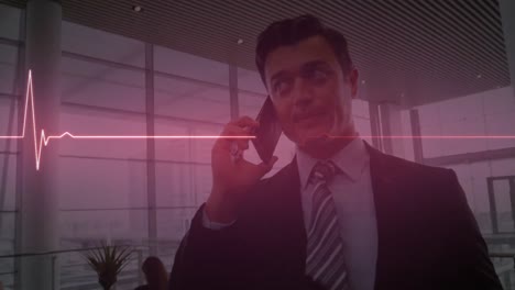 Animation-of-heart-monitor-against-caucasian-businessman-talking-on-smartphone-at-office