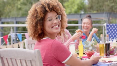 Portrait-of-biracial-woman-sitting-at-dinner-table-with-diverse-friends-in-garden,-slow-motion
