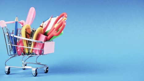 Close-up-of-shopping-trolley-with-school-items-and-copy-space-on-blue-background